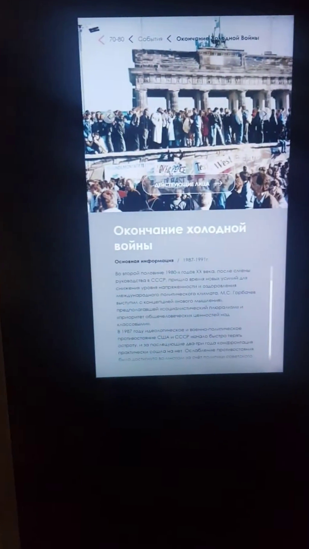Вертикальный сенсорный экран с приложением «Холодная война»: вверху снимок толпы на Берлинской стене у Бранденбургских ворот и кнопка «Действующие лица», ниже заголовок «Окончание холодной войны», годы 1987–1991 и текст справки