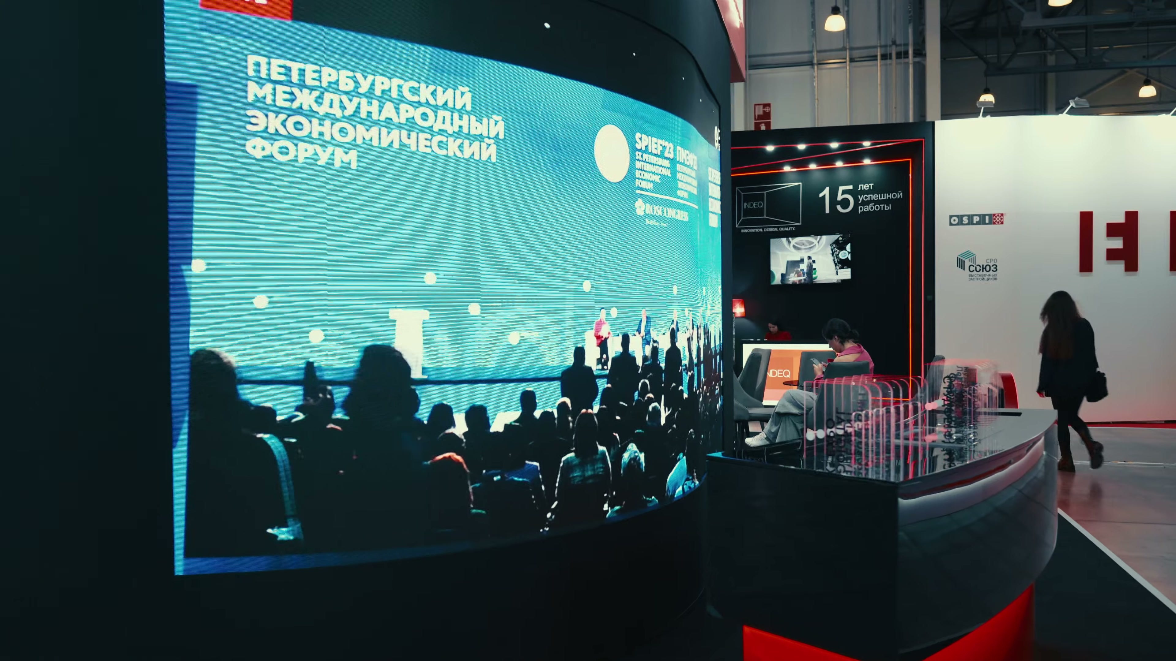 Изогнутый экран витрины с роликом о Петербургском международном экономическом форуме, справа — стойка с акриловыми карточками