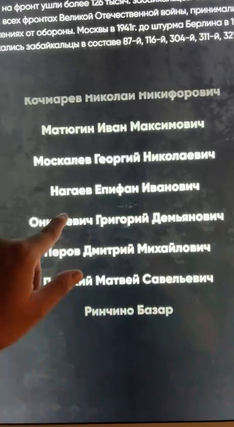 Список имён Героев Советского Союза на мультитач-панели, палец касается имени