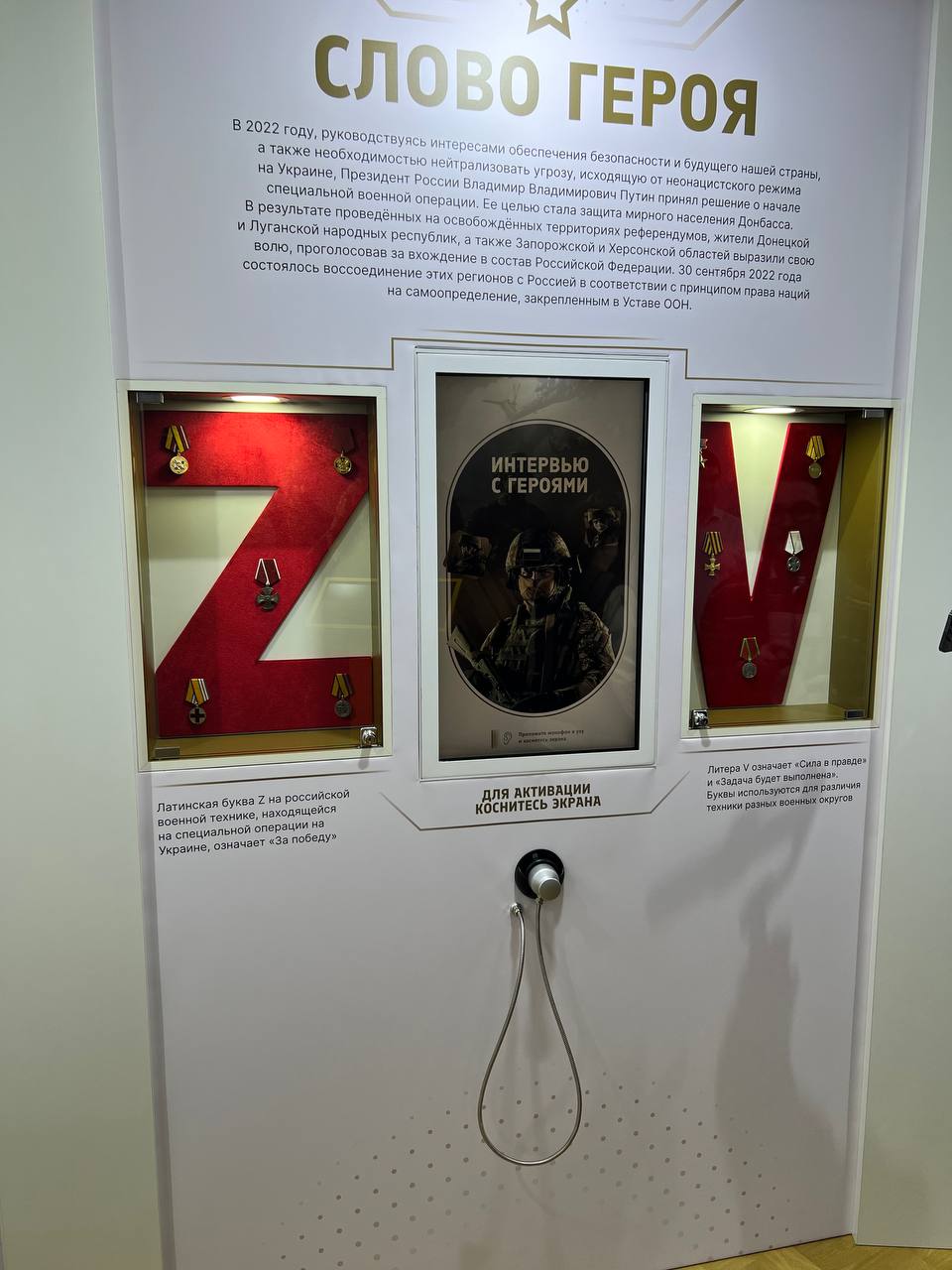 “A hero’s word” stand: text on the start of the special military operation; below, the red letters Z and V with medals and, between them, the vertical “Interviews with heroes” touch screen reading “Touch the screen to activate”, with a corded telephone handset beneath it