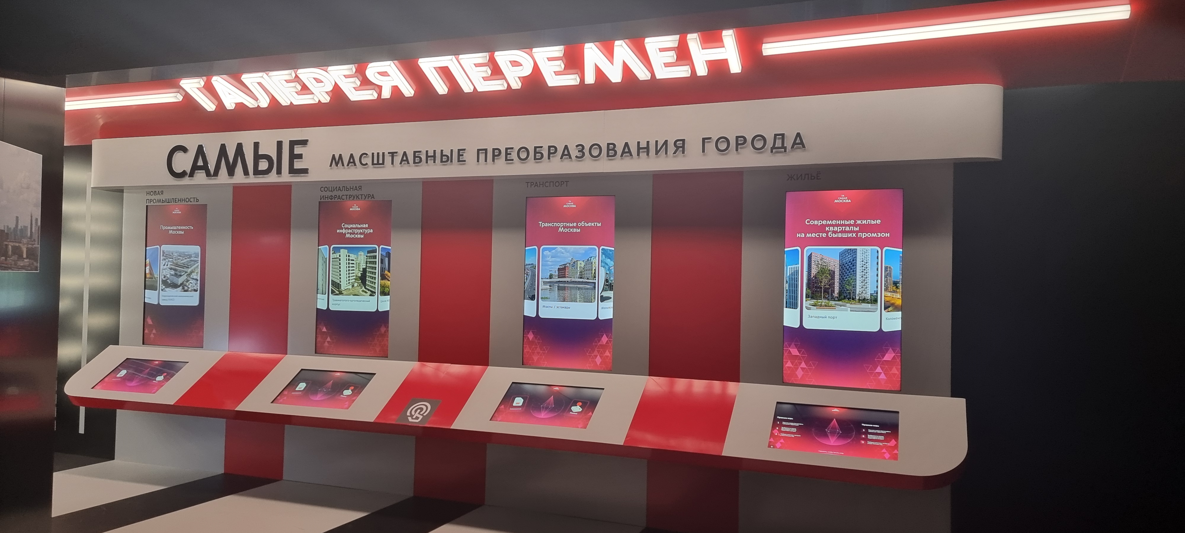 «Галерея перемен»: неоновая вывеска, стена «Самые масштабные преобразования города» и четыре стенда с вертикальными экранами и сенсорными панелями
