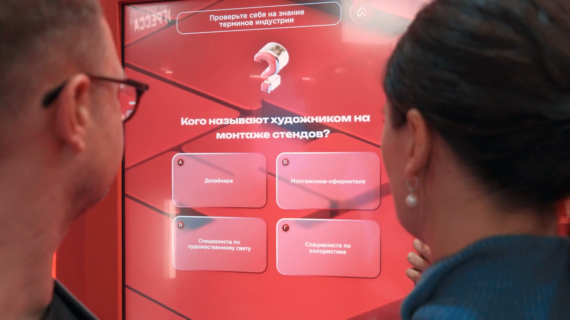 Двое посетителей у вертикального экрана квиза: вопрос «Кого называют художником на монтаже стендов?» и четыре варианта ответа