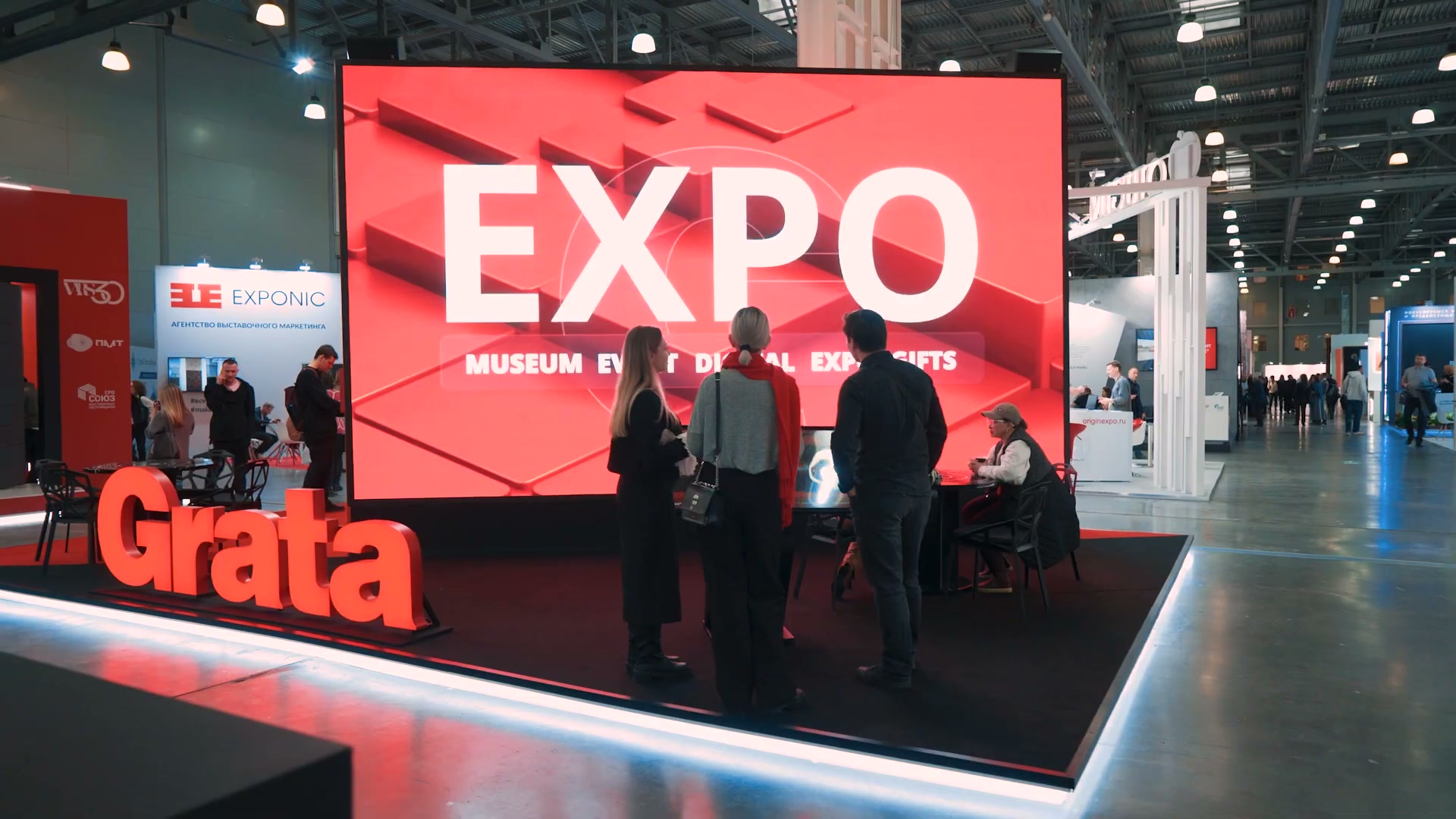 Стенд со стороны прохода: большой светодиодный экран с заставкой EXPO, перед ним гости у сенсорного стола