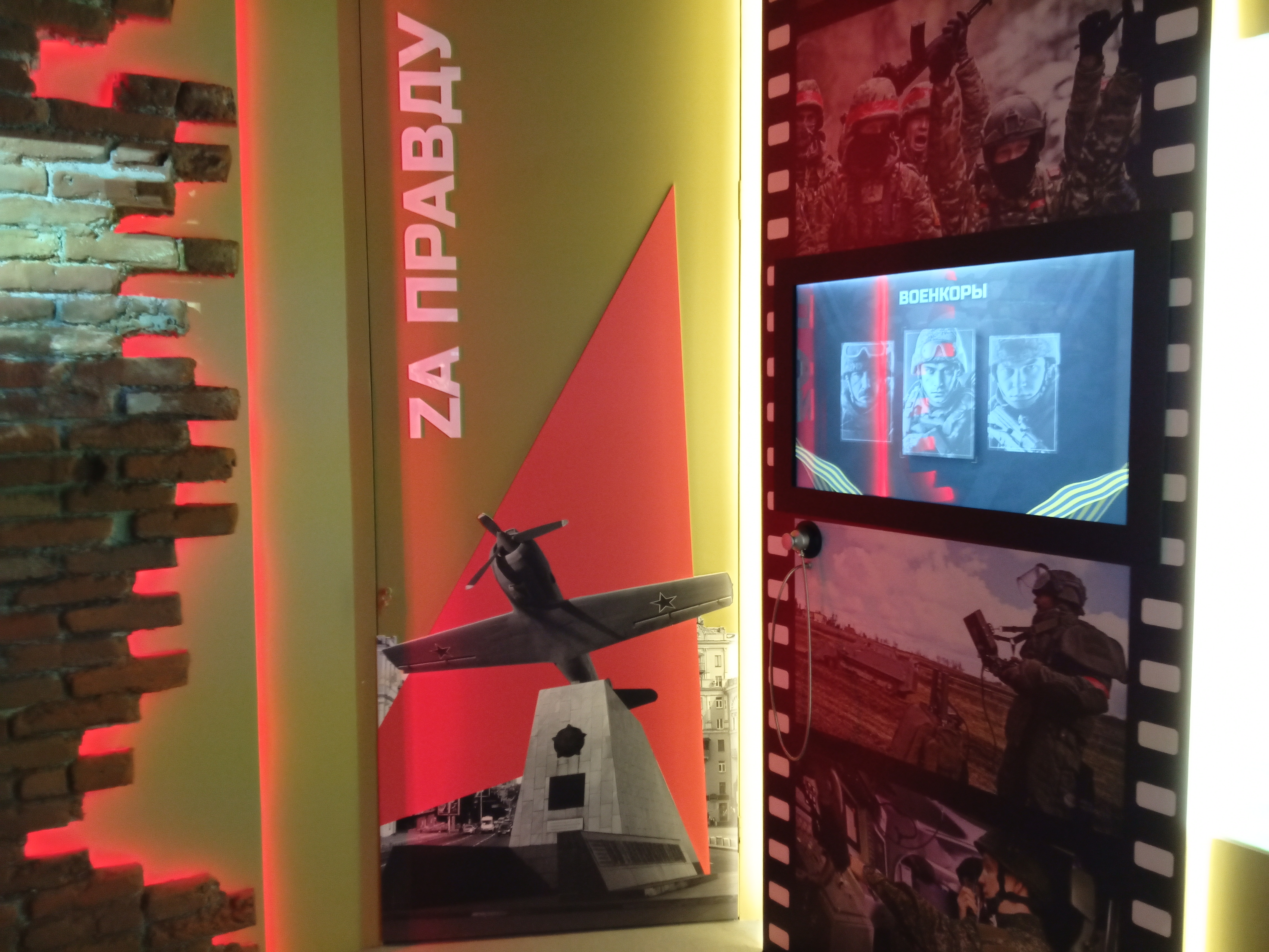 Экран с заголовком «Военкоры» и тремя портретами, встроенный в панно-«киноленту», рядом на стене — монофон