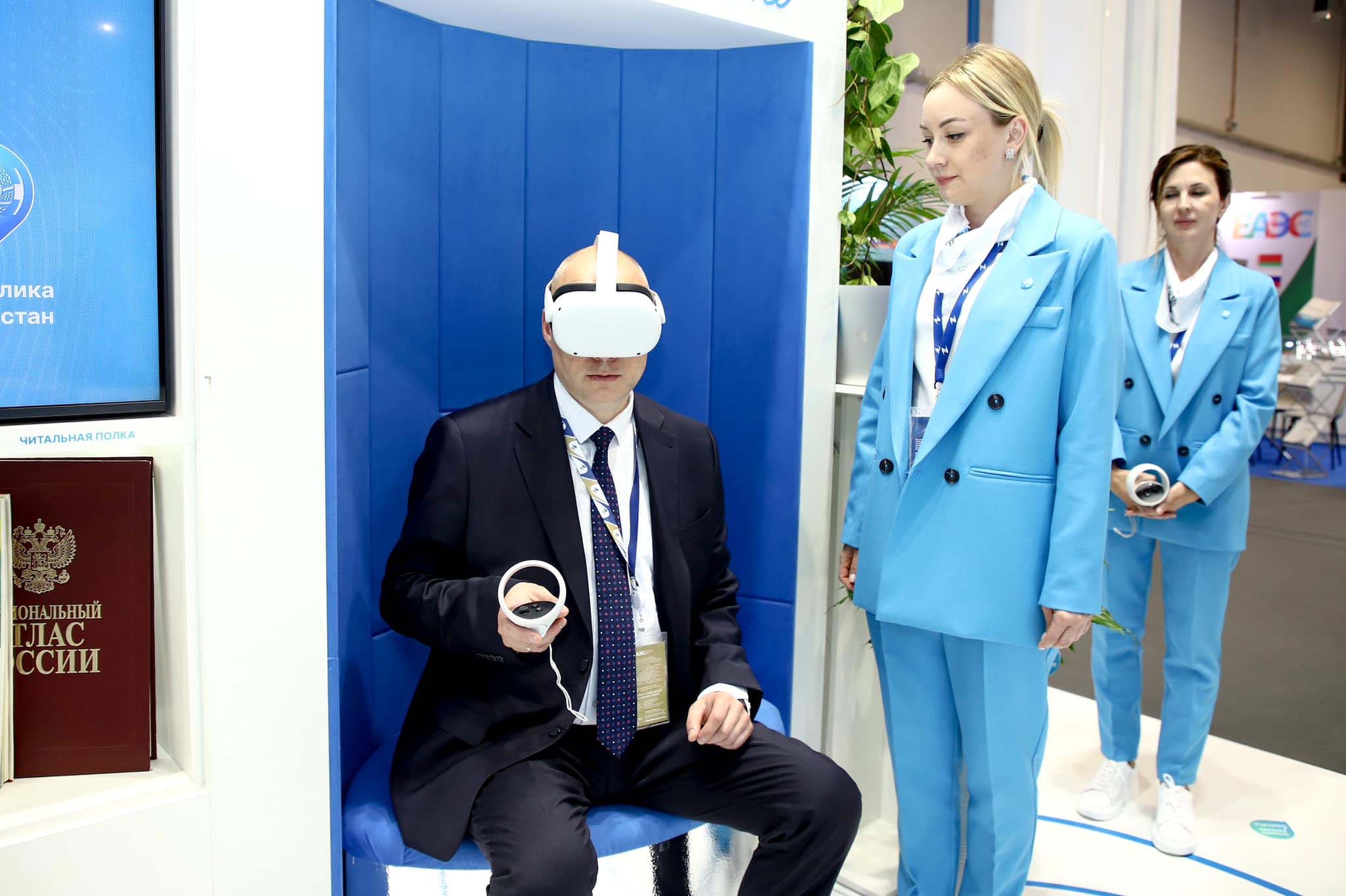 A guest in a VR headset with a controller, stand staff beside him