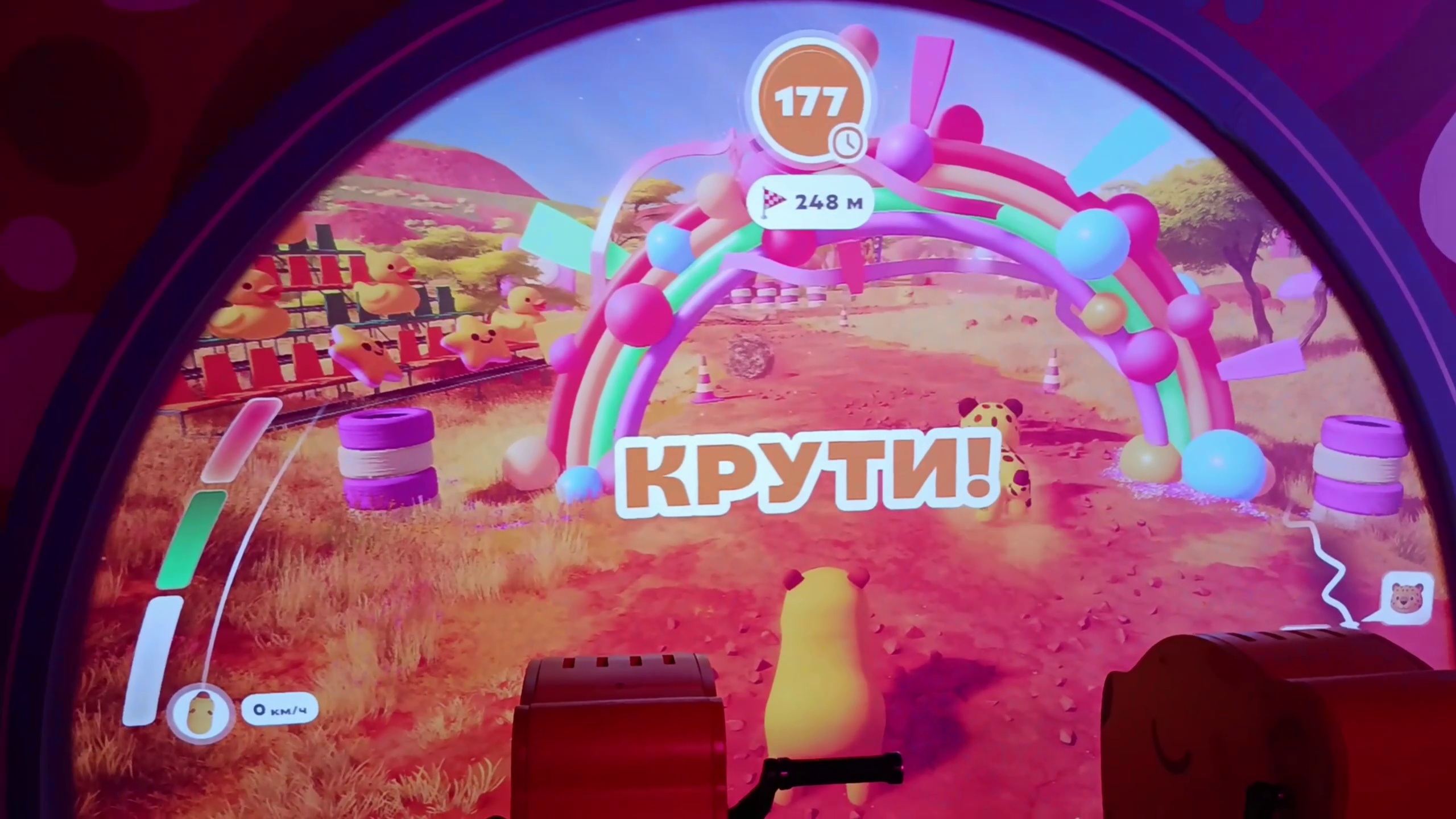 The “Capy and Leo” race on an arched projection: a capybara by a rainbow arch; in the foreground, the stands with handles that players turn to speed up the characters