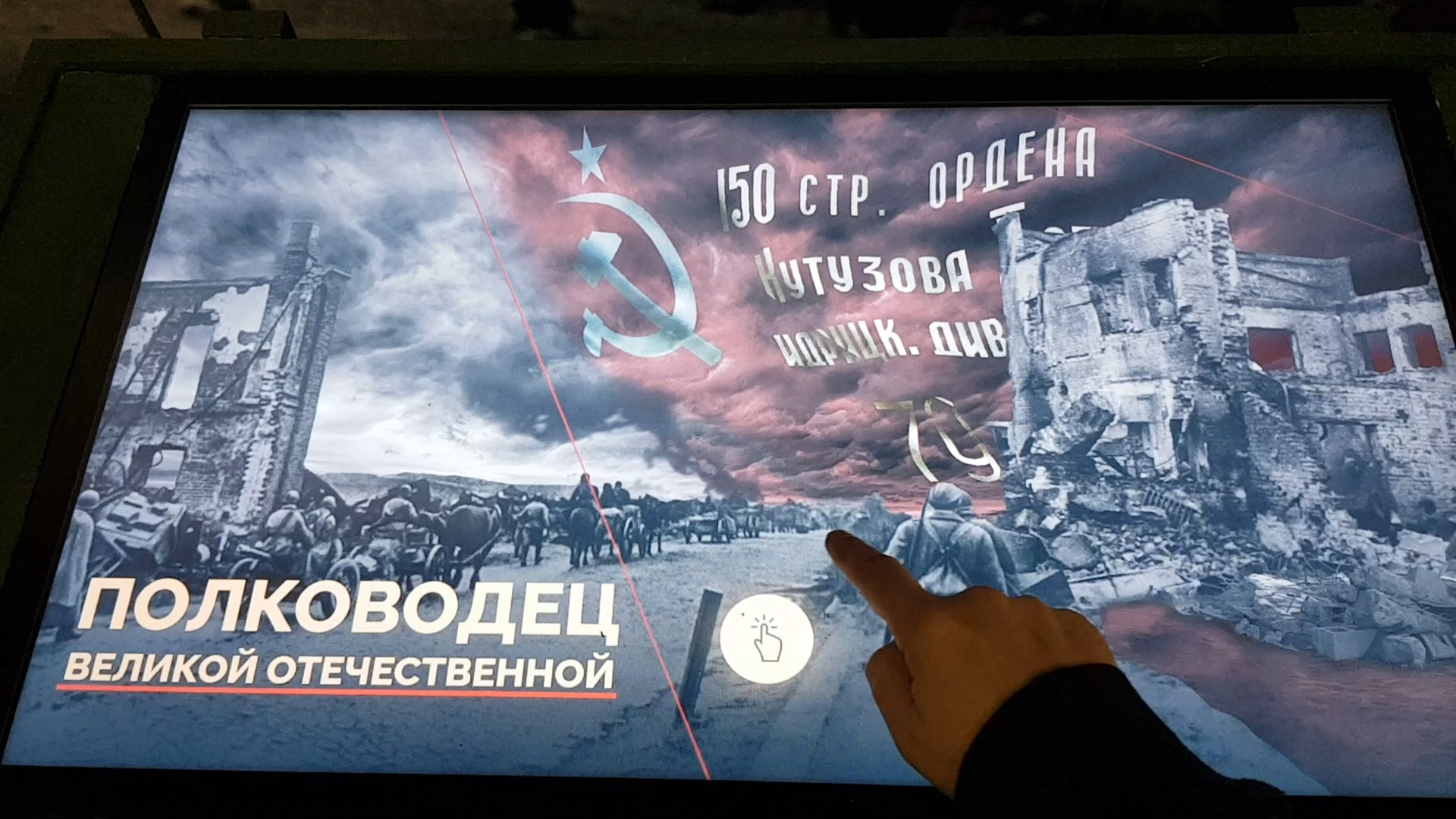 Посетитель касается экрана стола в корпусе из оружейных ящиков; на заставке надпись «Полководец Великой Отечественной» поверх архивного снимка