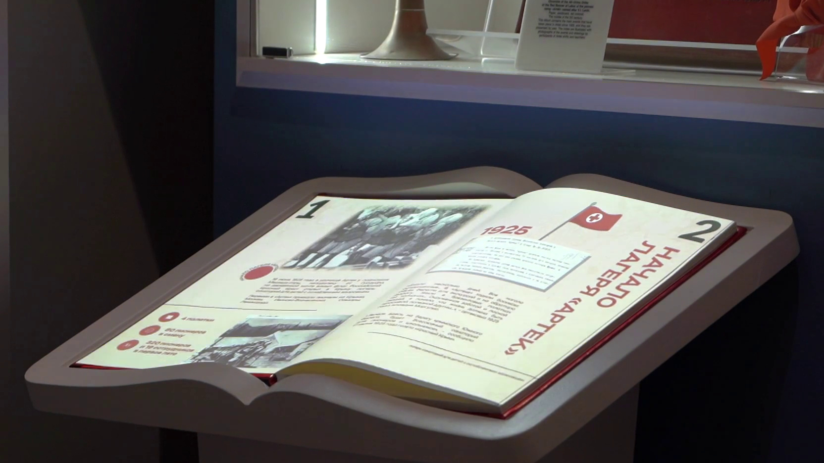 Проекционная книга на стойке: разворот «1925. Начало лагеря „Артек“», за ней — витрина с подсветкой