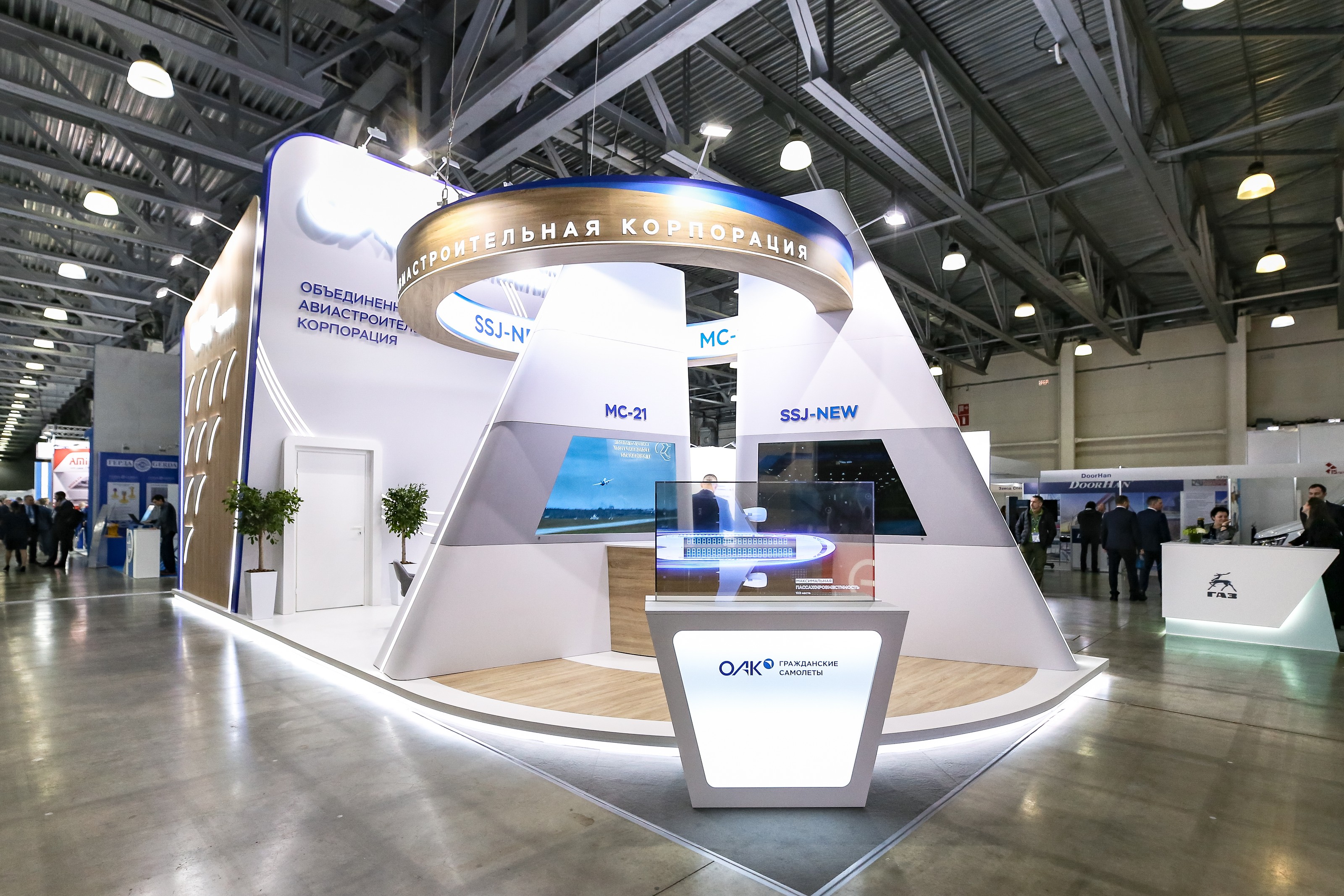 Стенд корпорации «Иркут» на NAIS 2023: тумба с прозрачным экраном перед колоннами «МС-21» и «SSJ-NEW»