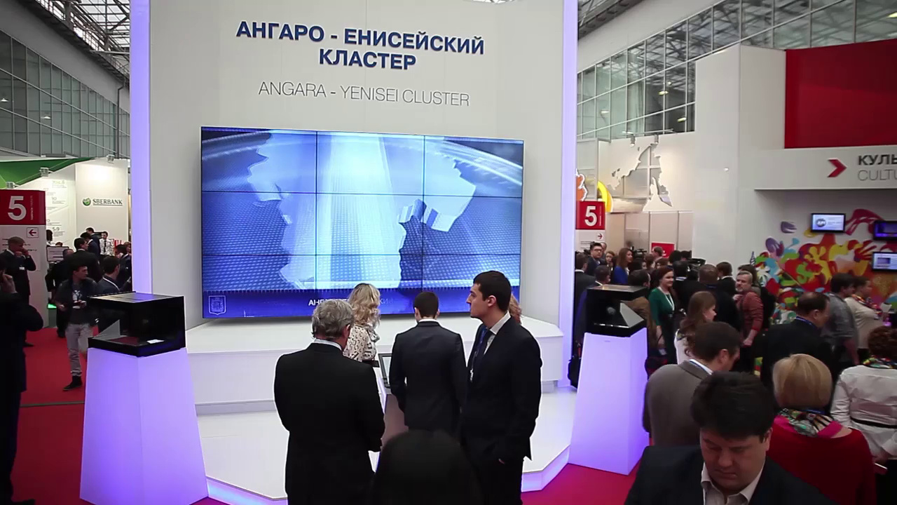Белый стенд «Ангаро-Енисейский кластер» с видеостеной, пультом и двумя пирамидами, вокруг посетители форума
