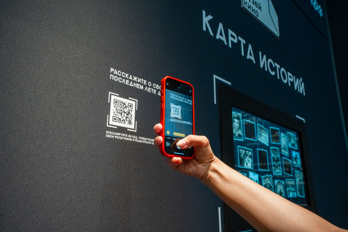 Рука с телефоном сканирует QR-код на стене «Карта историй», справа экран с фотографиями