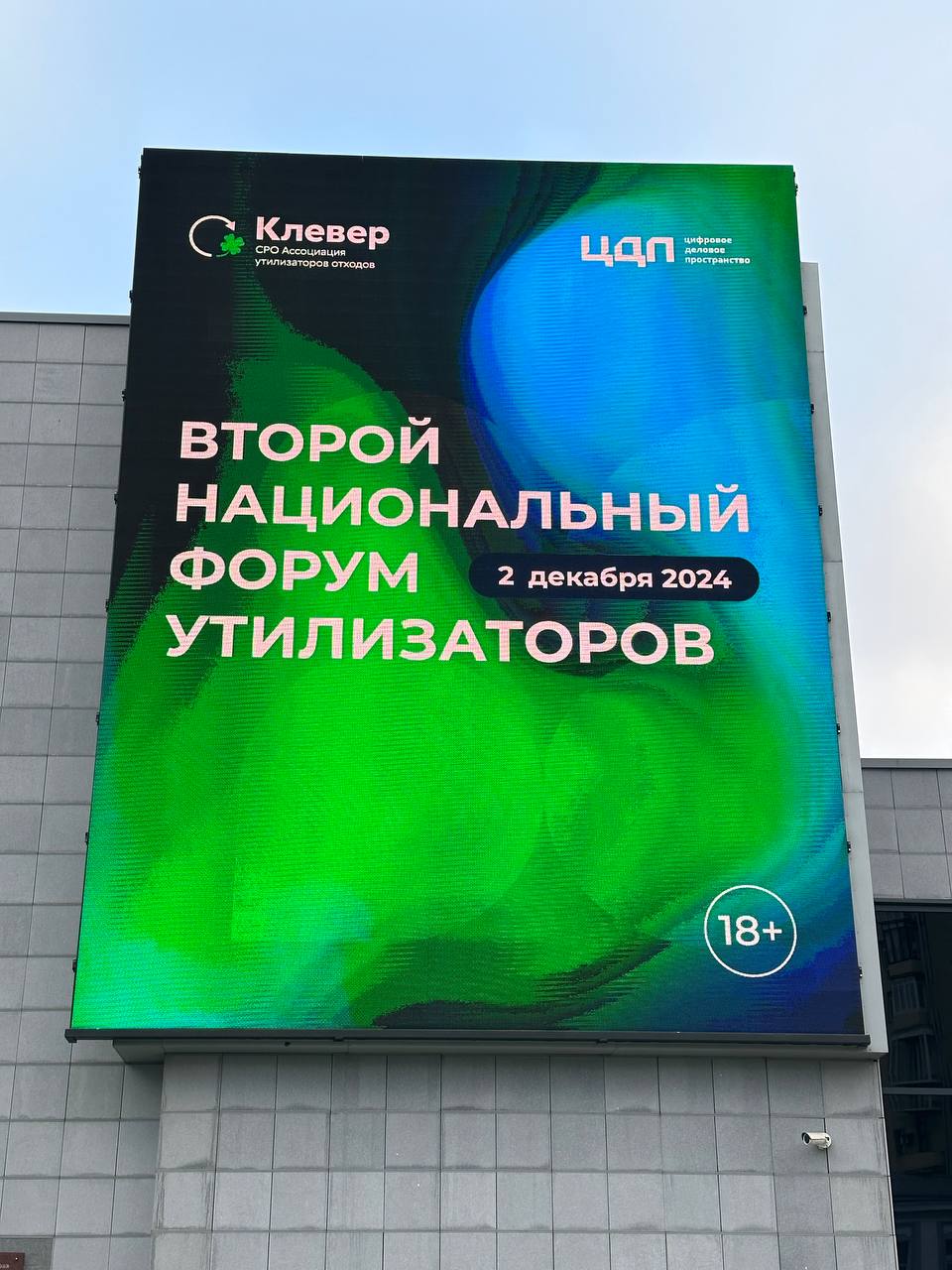 Vertical LED media facade on the DBS wall, seen head-on from below: the words “Second National Forum of Recyclers”, a “2 December 2024” badge, the Klever and DBS logos and an 18+ sign on a green-blue background