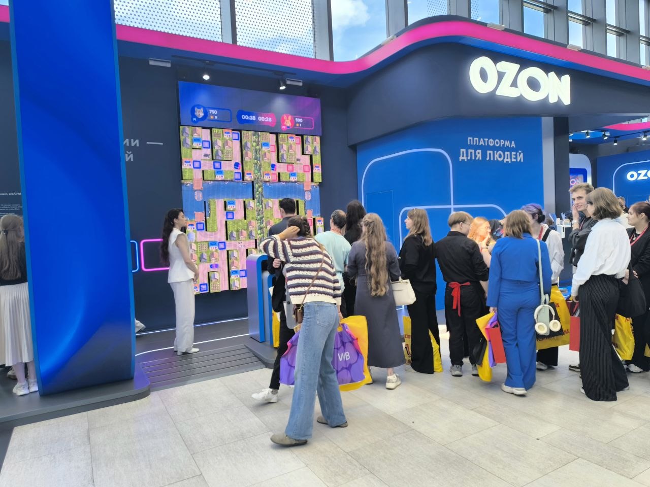 Очередь к игре у стенда Ozon; на экране — уровень с деревнями