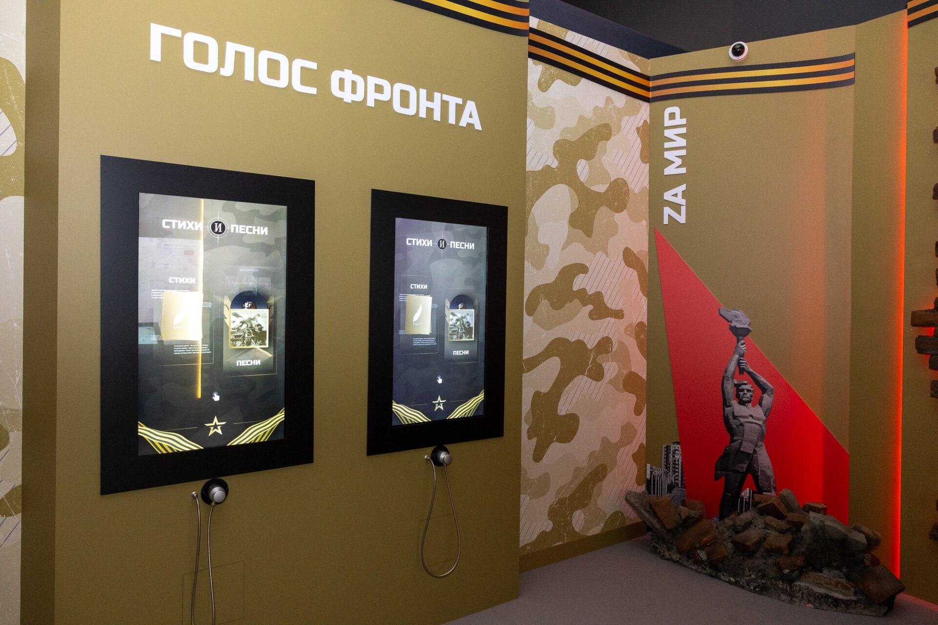 Стена раздела «Голос фронта» с двумя вертикальными сенсорными экранами «Стихи и песни», под каждым — монофон на шнуре