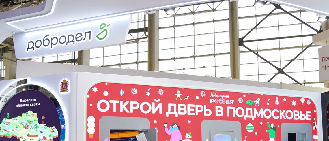 Фасад стенда в декабре 2023 года: красный новогодний рисунок, знак «Новогодняя Россия» и надпись «Открой дверь в Подмосковье» над тремя дверями, слева — круглый экран с картой области